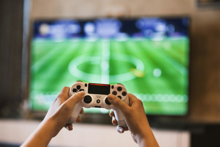Person Holding Game Pad in front of Big TV showing Football Match
